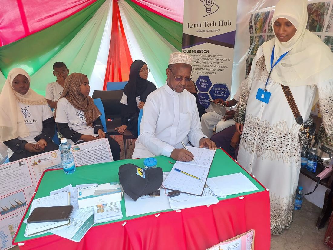 Guest signing the visitors' book at the Lamu Tech Hub stand, with students