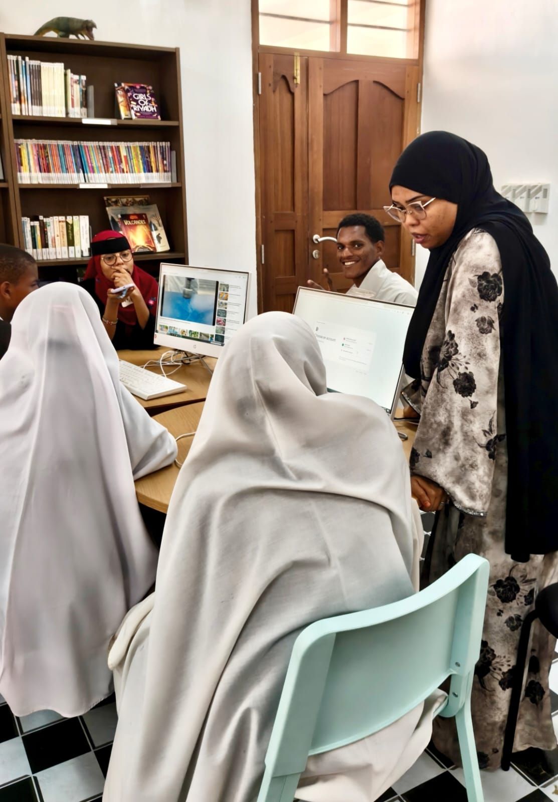 Mentor guiding Technovation students working on computers in a Lamu library